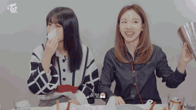two girls are sitting at a table with a twice logo on the bottom