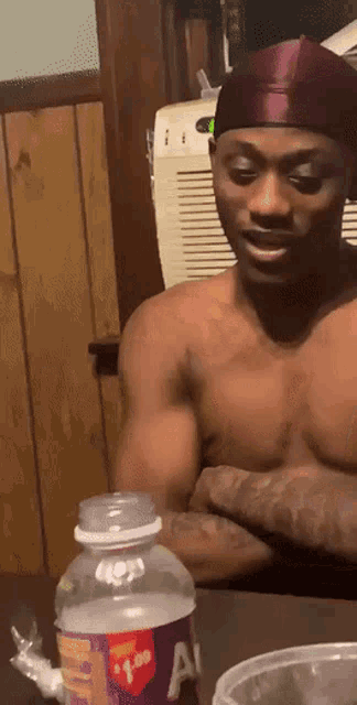 a shirtless man sits at a table next to a bottle of a1 juice