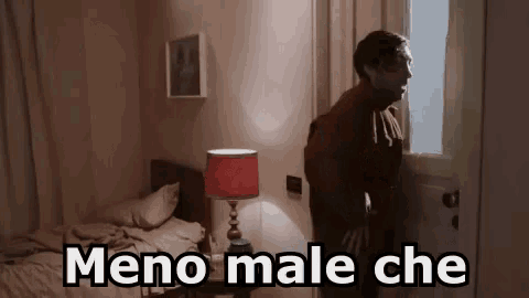 a man is standing in a bedroom with a lamp and a bed and the words meno male che written on the door .