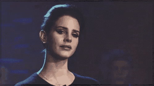 a woman in a black shirt is smiling and looking at the camera in a dark room .
