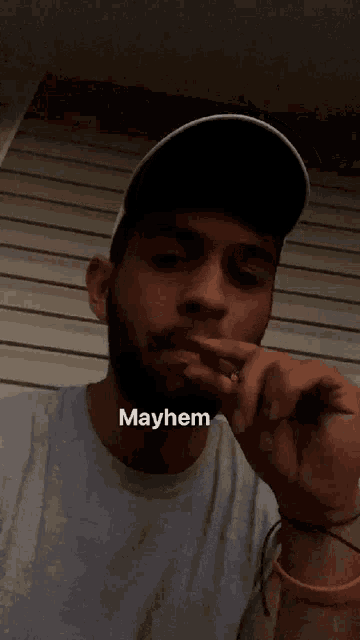 a man with a beard is smoking a cigarette and his shirt says mayhem on it
