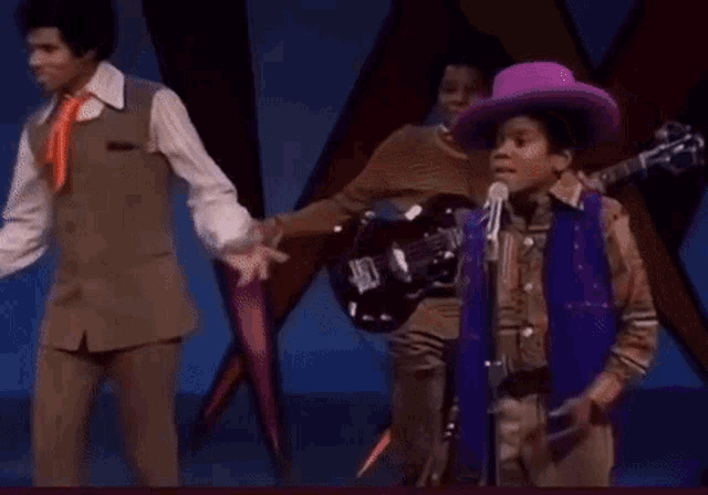 a man in a purple hat is singing into a microphone while another man plays a guitar