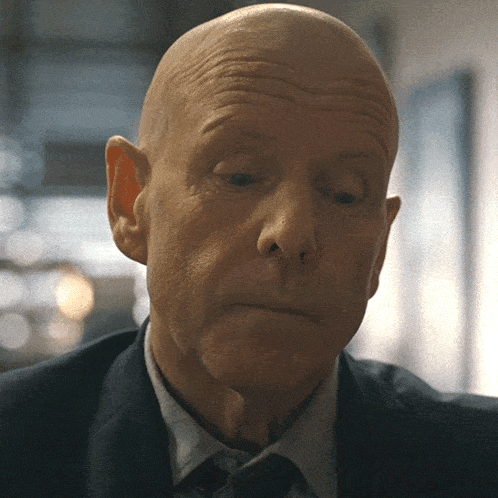 a bald man in a suit and tie looks down
