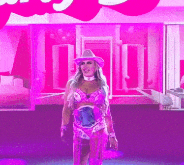 a woman in a cowboy hat stands in front of a pink wall