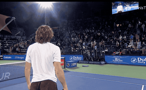 a man stands on a tennis court with dubai duty free banners