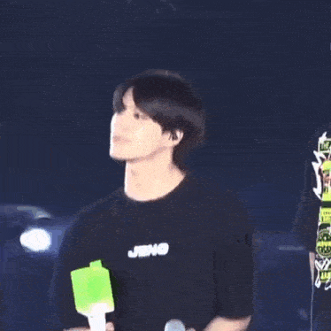 a man in a black shirt is holding a microphone and a green stick .