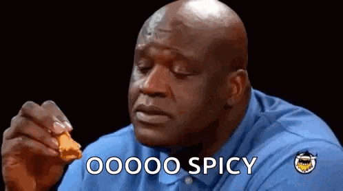 a bald man in a blue shirt is eating a piece of chicken and saying `` oooo spicy '' .