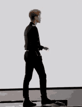 a man in a black suit is walking on a treadmill in front of a white wall .