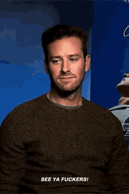 a man in a brown sweater is smiling and talking .