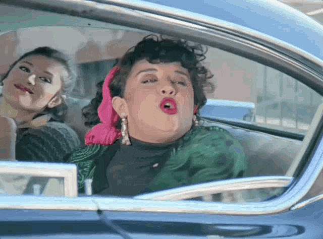 two women are sitting in a car and one is making a face