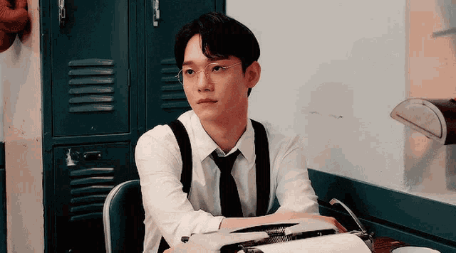 a young man wearing glasses and suspenders is sitting at a table with a typewriter