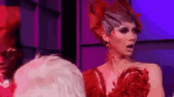 a drag queen wearing a red dress and a crown is standing in front of a group of people .