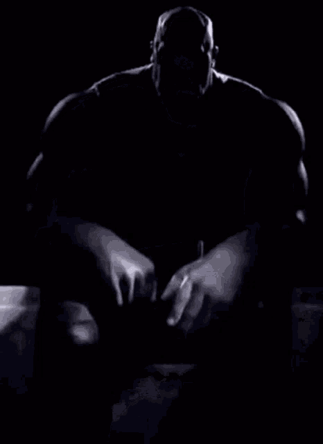 a bald man with a beard is sitting down with his hands folded in front of him .