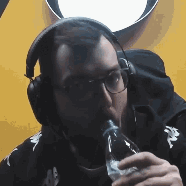 a man wearing headphones and glasses is drinking from a plastic bottle