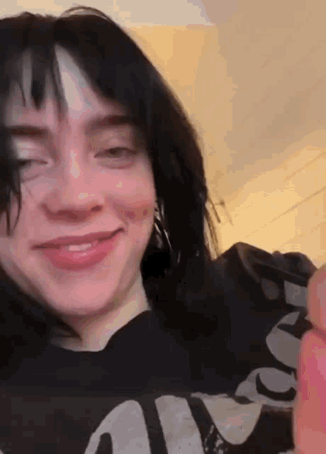 billie eilish is wearing a black shirt and smiling while holding a red object .