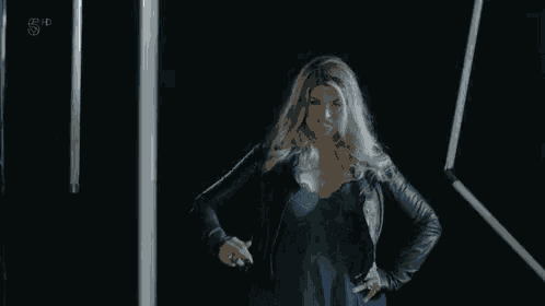 a woman in a blue dress and black leather jacket is standing in front of a wall of lights .