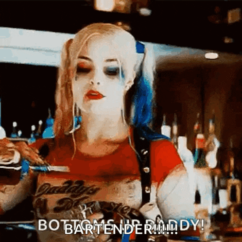 a woman in a harley quinn costume is standing at a bar holding a drink .