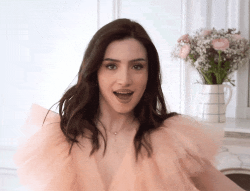 a woman in a pink ruffled top is standing in front of a vase of baby 's breath flowers