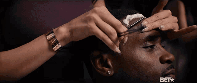 a woman shaves a man 's forehead with a razor and a bet logo in the corner