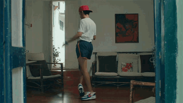 a man wearing shorts and a red hat stands in a living room