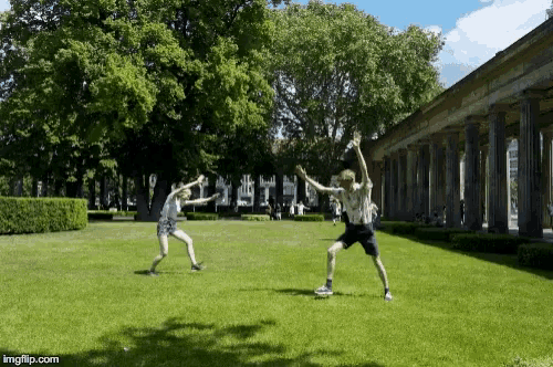 a man and a woman are playing frisbee in a park with imgflip.com