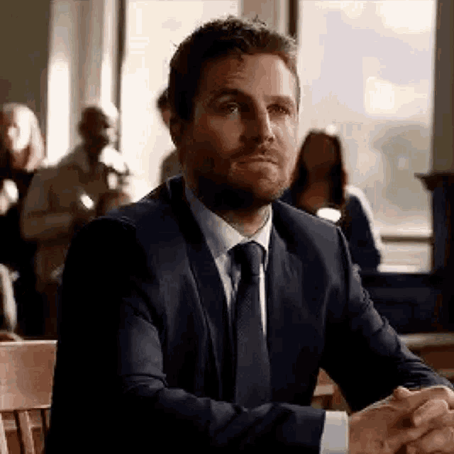 a man in a suit and tie is sitting in a courtroom .