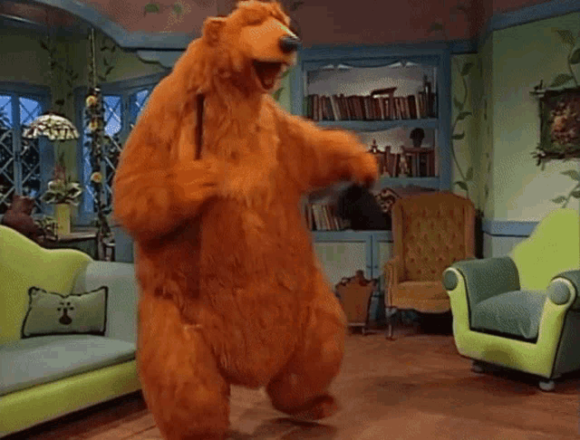 a teddy bear is dancing in a living room with a couch and chair