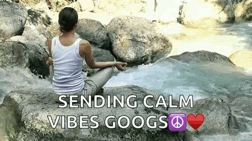 a woman is sitting on a rock in front of a river and sending calm vibes .