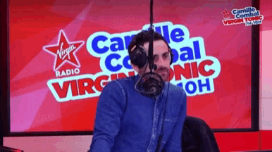 a man wearing headphones is in front of a virgin radio sign