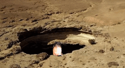 a large hole in the ground in the middle of a desert with a flame coming out of it .