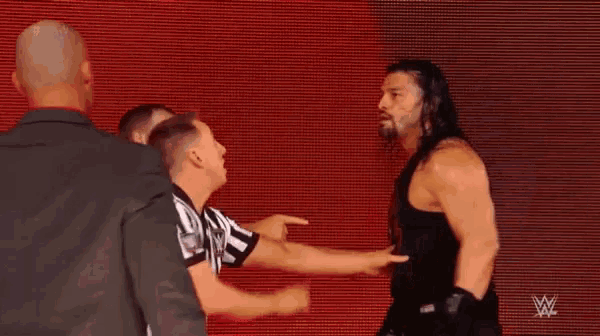 a referee is pointing at a wrestler who is standing in front of a red background .