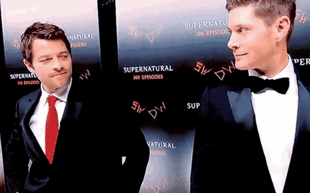 two men in tuxedos are standing next to each other in front of a sign that says supernatural
