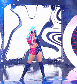 a woman in a crop top and shorts is dancing on a stage in front of a large x