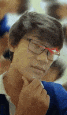 a young boy wearing glasses and a blue shirt holds his hand to his chin
