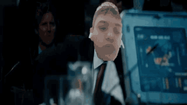 a man in a suit and tie is sitting in front of a computer screen with his eyes closed .