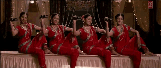 a group of women in red dresses are sitting next to each other on a stage .