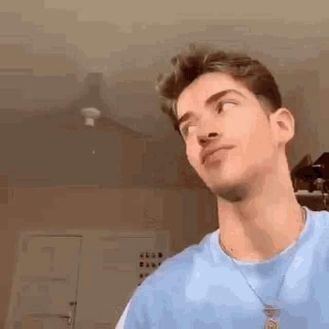 a young man wearing a blue shirt and a necklace is looking up at the ceiling .