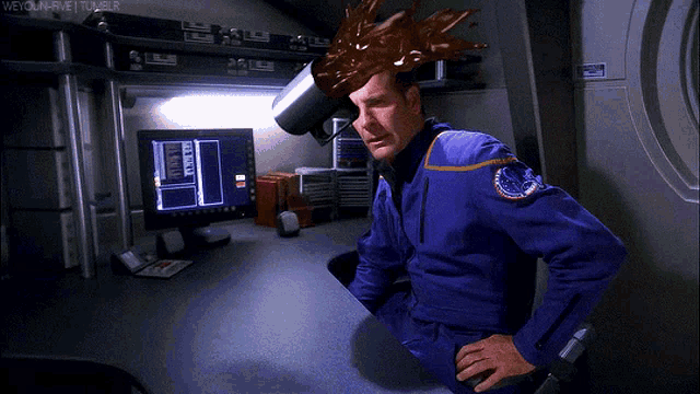 a man in a blue uniform is sitting at a desk with a coffee mug on his head