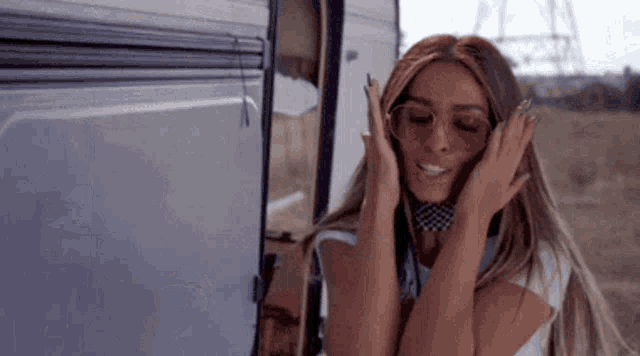 a woman wearing sunglasses and a bandana is standing in front of a trailer in the desert .