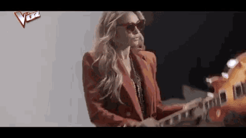 a woman wearing sunglasses and a red jacket is playing a guitar .