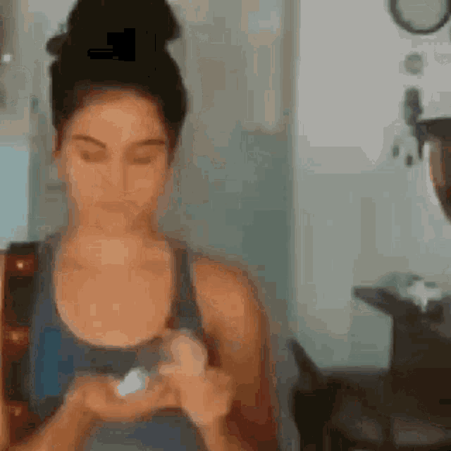 a woman in a blue tank top is holding a small object in her hands .