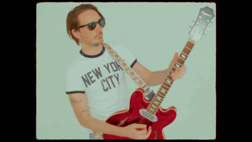 a man in a new york city shirt is holding a red guitar