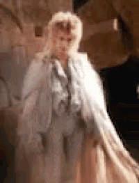 a woman in a white coat is standing in front of a brick wall .