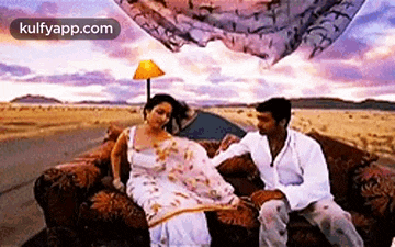 a man and a woman are sitting on a couch in the middle of a desert .