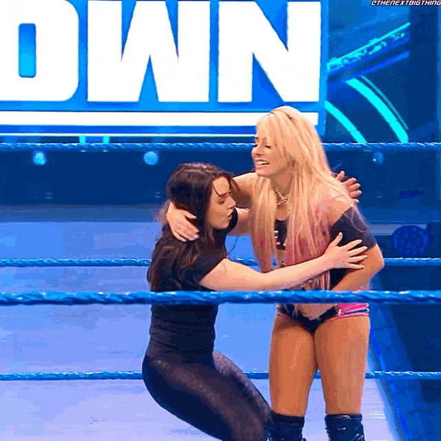 a woman is hugging another woman in a wrestling ring with the word own behind them