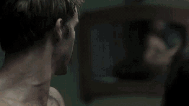 a man without a shirt is looking at his reflection in a mirror