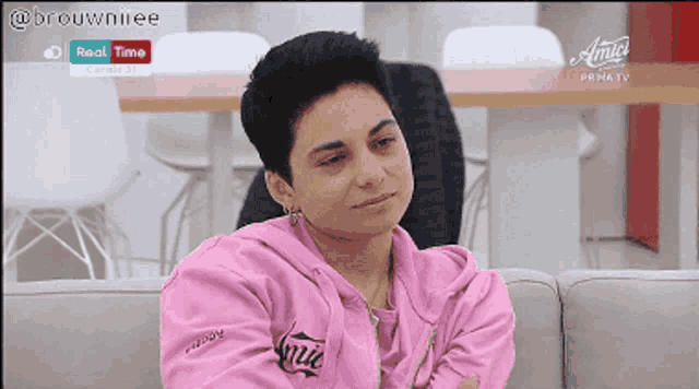 a woman is sitting on a couch wearing a pink hoodie that says amici on it