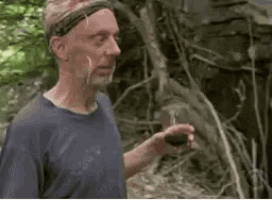 a man in a blue shirt is holding a glass of wine in the woods .