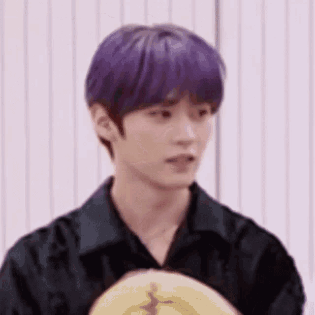 a young man with purple hair is wearing a black shirt and holding a yellow object .