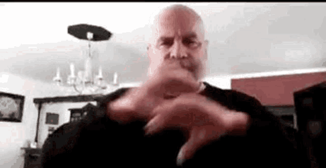 a bald man with a beard is making a heart with his hands .